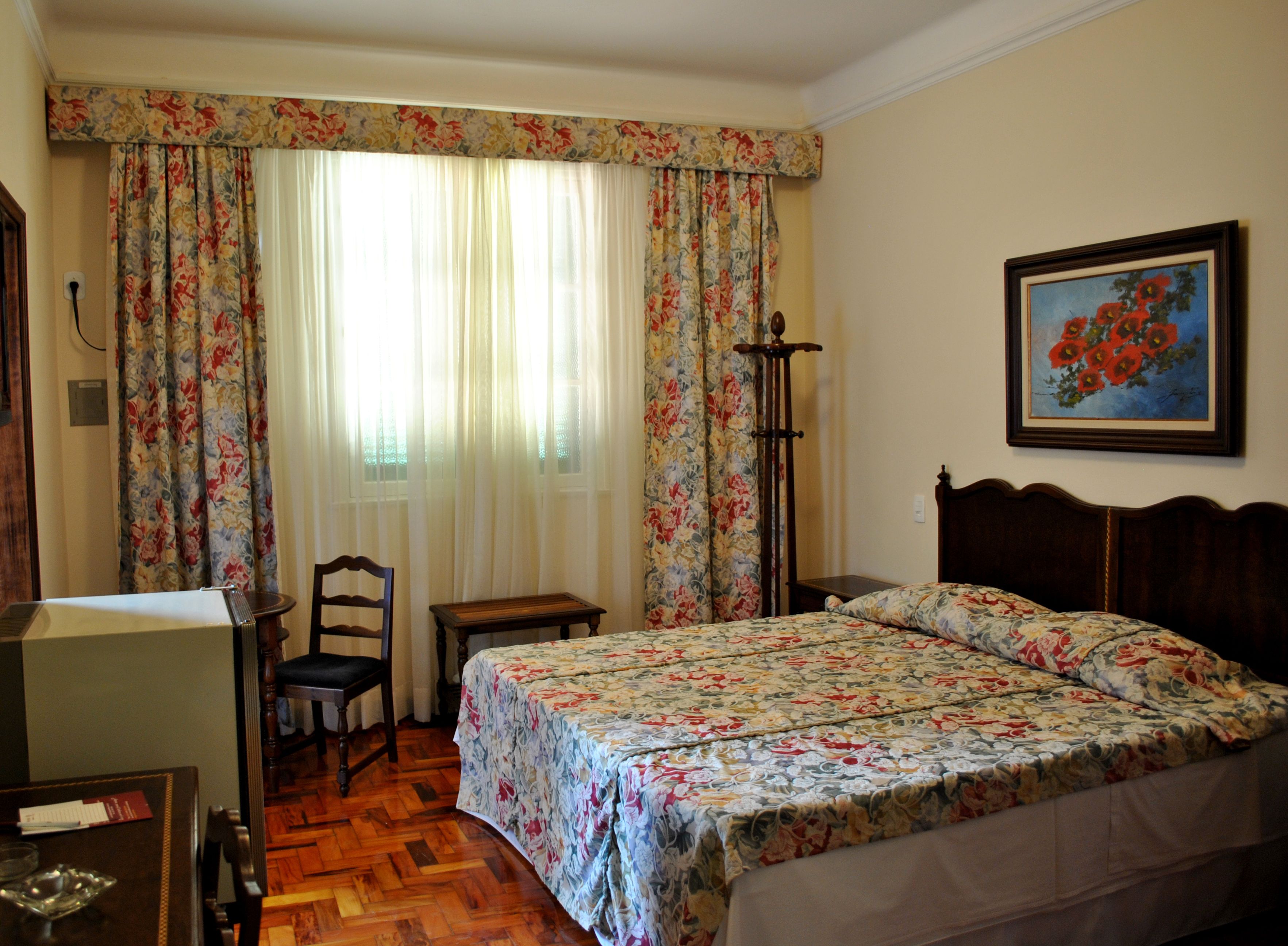 A bedroom with a wooden bed, a desk, a chair, and a bedside table.