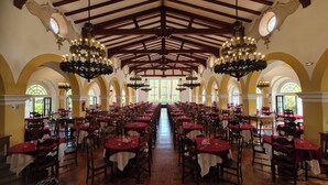 A large banquet hall with high ceilings, chandeliers, and arched windows. Tables are set with red tablecloths and white table runners. - Glória Caxambu Resort & Convention (Caxambu)