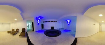 Uma área moderna de piscina interna com uma banheira de hidromassagem circular, espreguiçadeiras e iluminação azul ambiente.