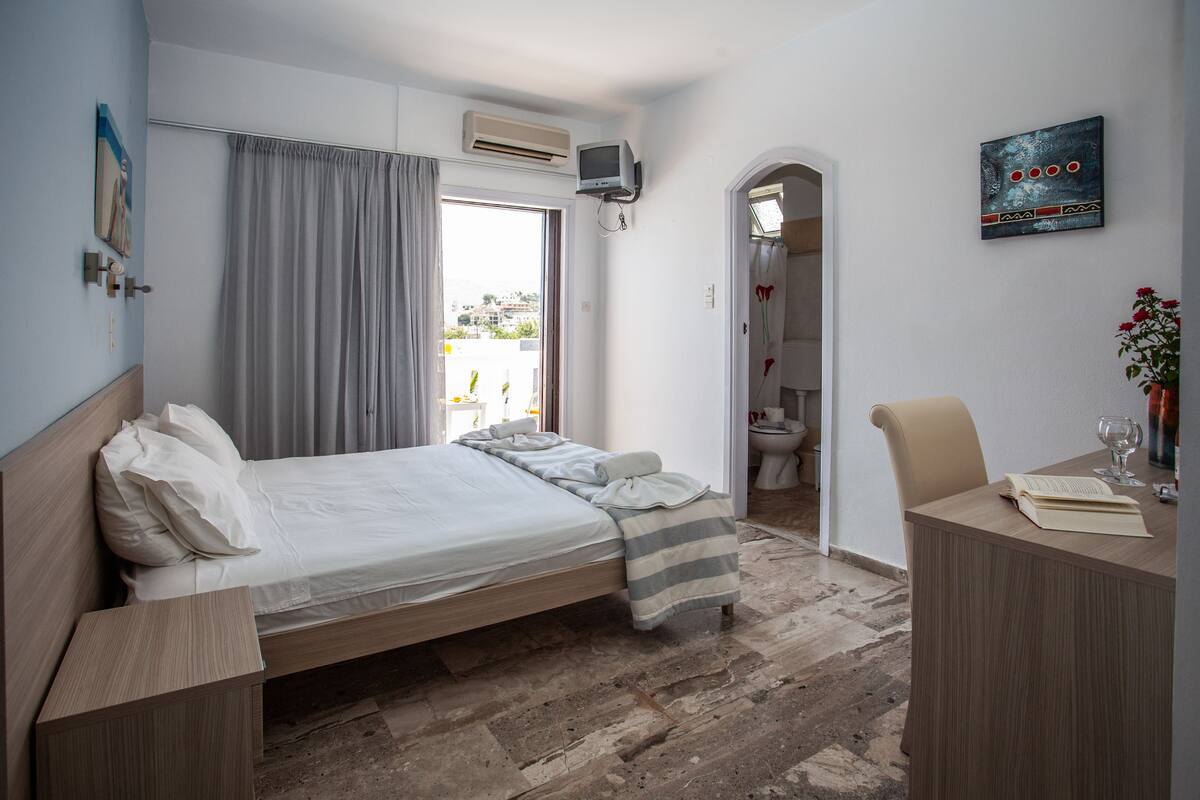 A bedroom with a bed, a desk, and a bathroom visible through an open door.
