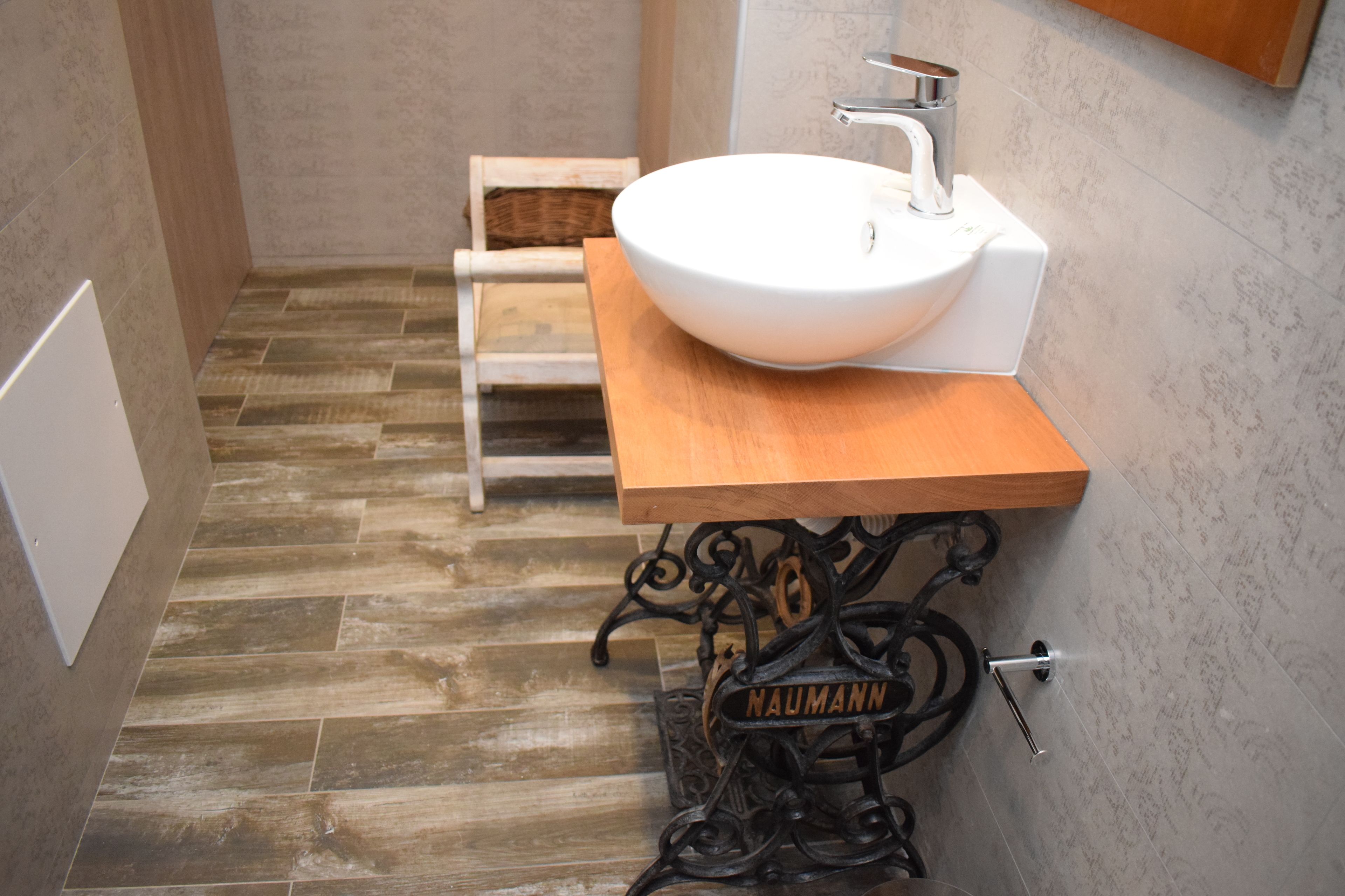 Un baño con un lavabo blanco sobre una encimera de madera, una base de hierro forjado negro con el nombre "NAUMANN" y un banco de madera al fondo.