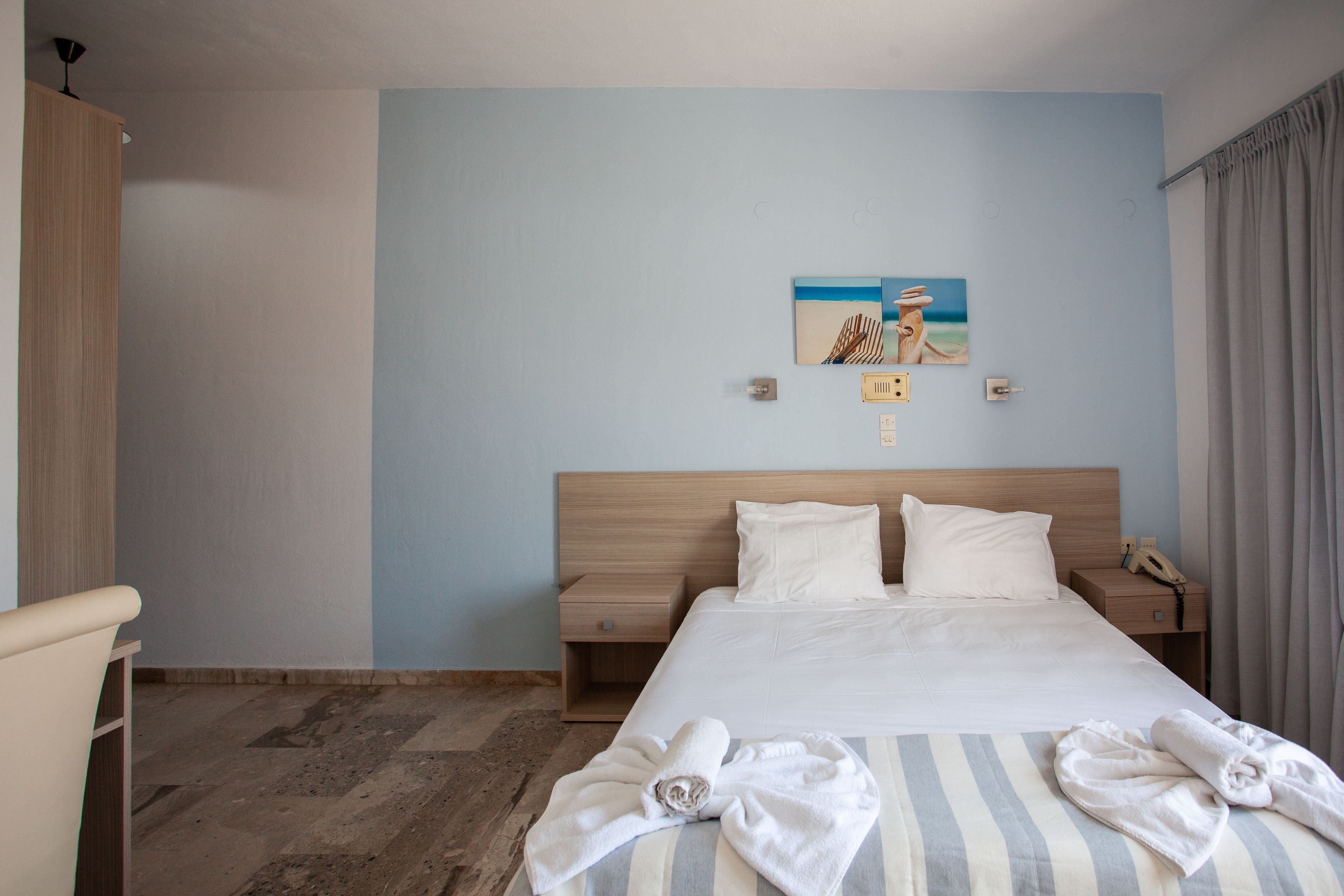 A hotel room with a large bed, two bedside tables, a wooden wardrobe, and a painting on the wall.