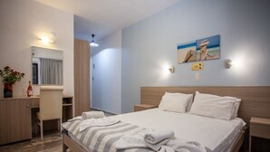 A hotel room with a bed, bedside table, a desk with a chair, a mirror, and a wall-mounted light fixture. - Myrtis (Agios Vasileios)