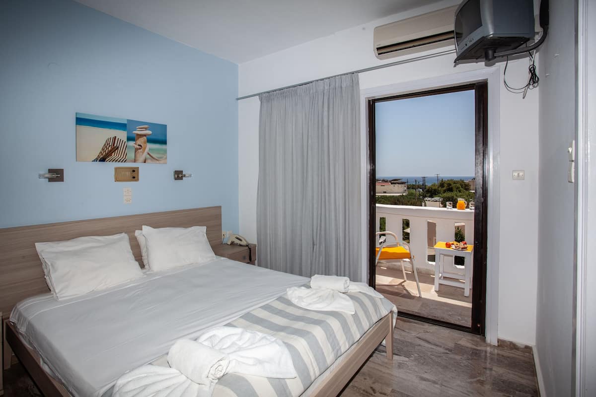 A hotel room with a bed, a painting, a curtain, and a view of the outside.