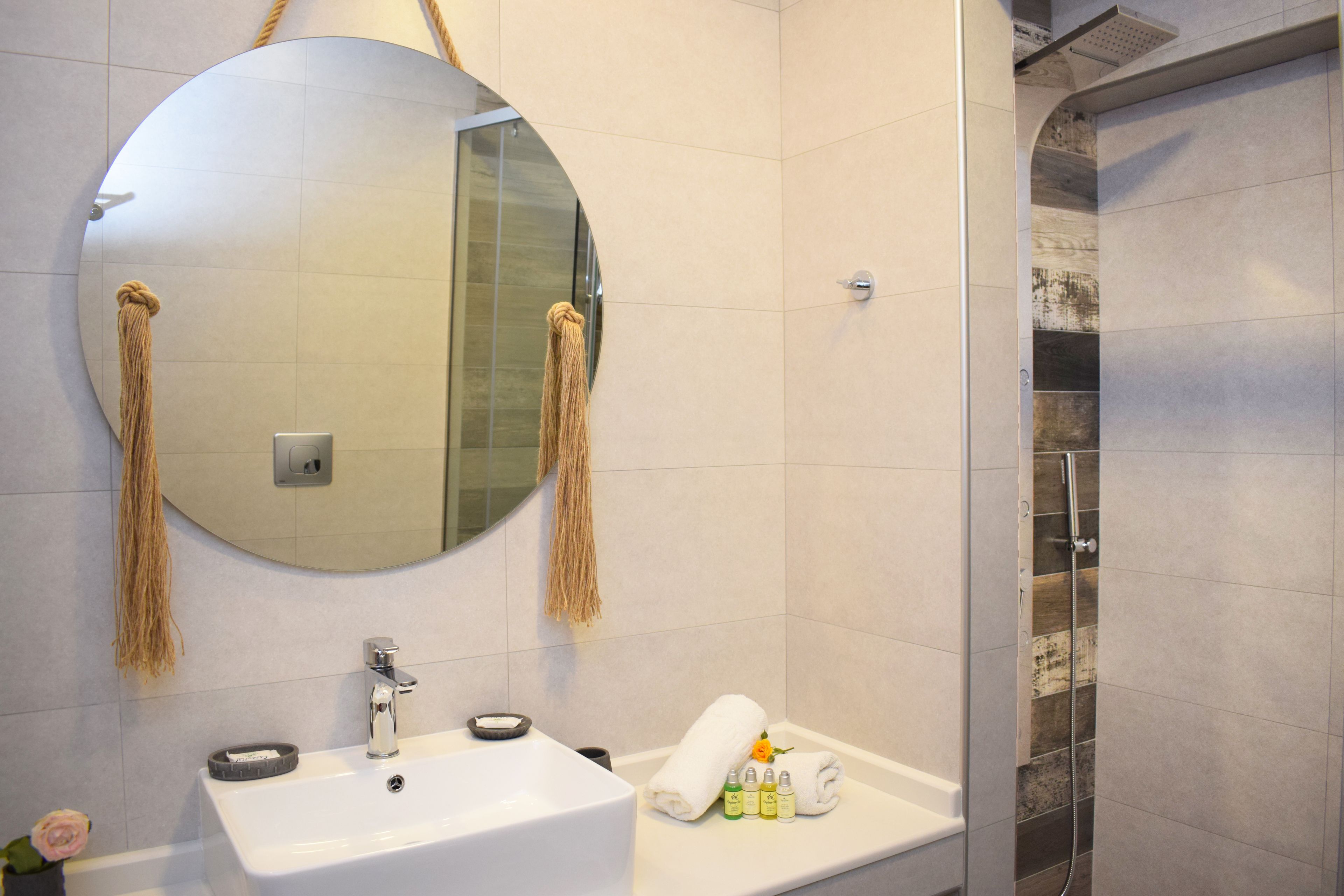 A bathroom with a round mirror, a sink, a towel, and toiletries.