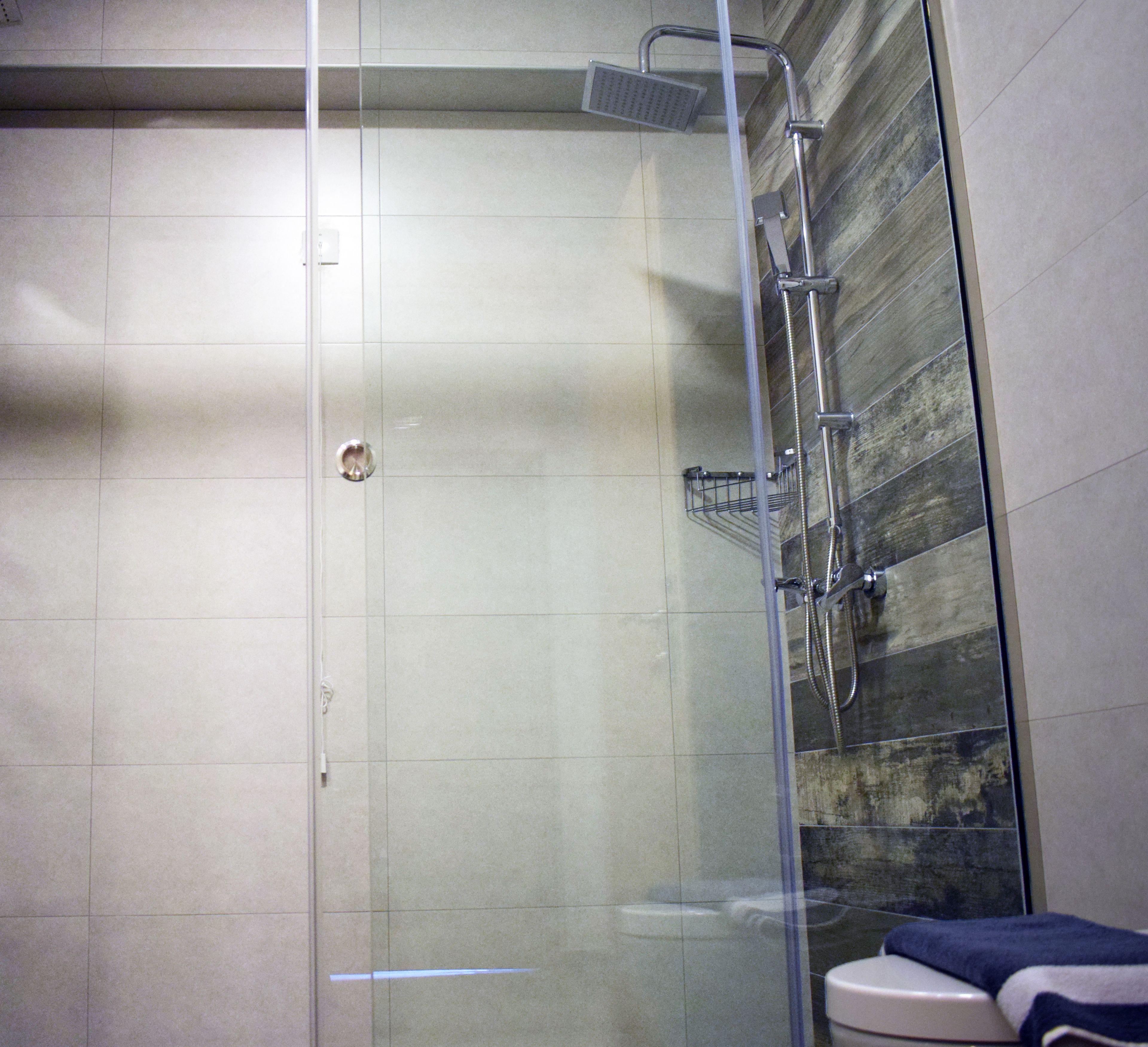 A glass-enclosed shower with a handheld showerhead and a wall-mounted faucet.