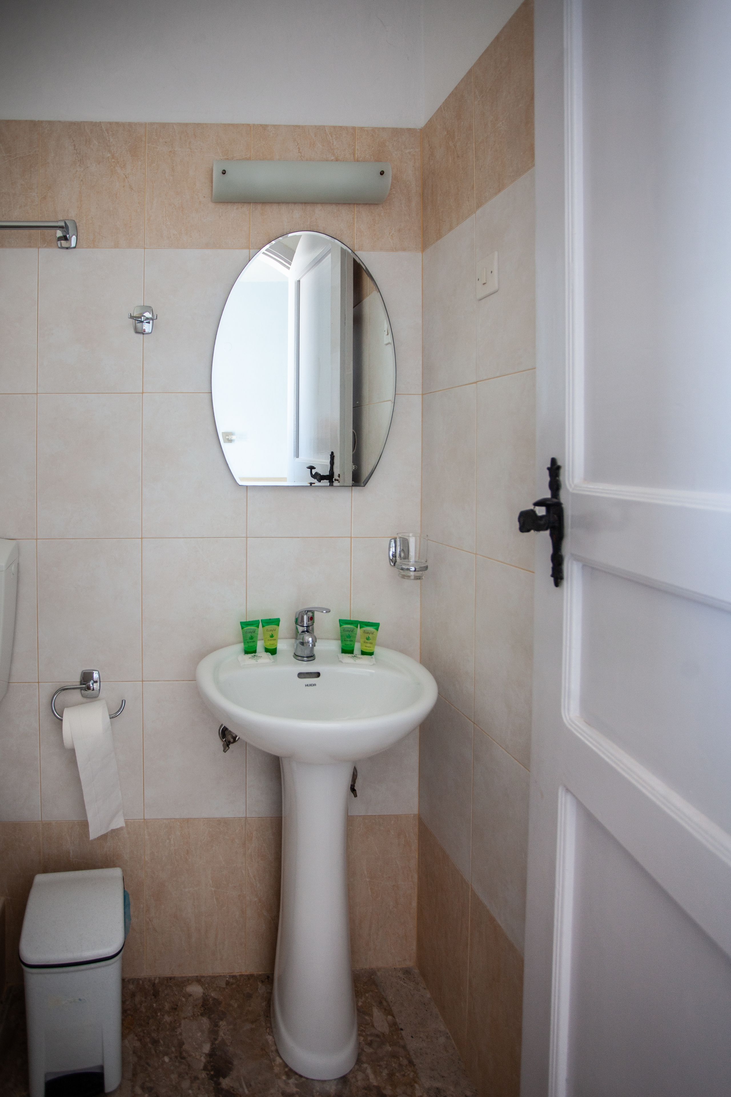 A bathroom with a pedestal sink, a toilet, a mirror, and a towel rack.