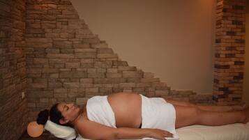 A person lying on a massage table in a room with stone walls and a staircase.