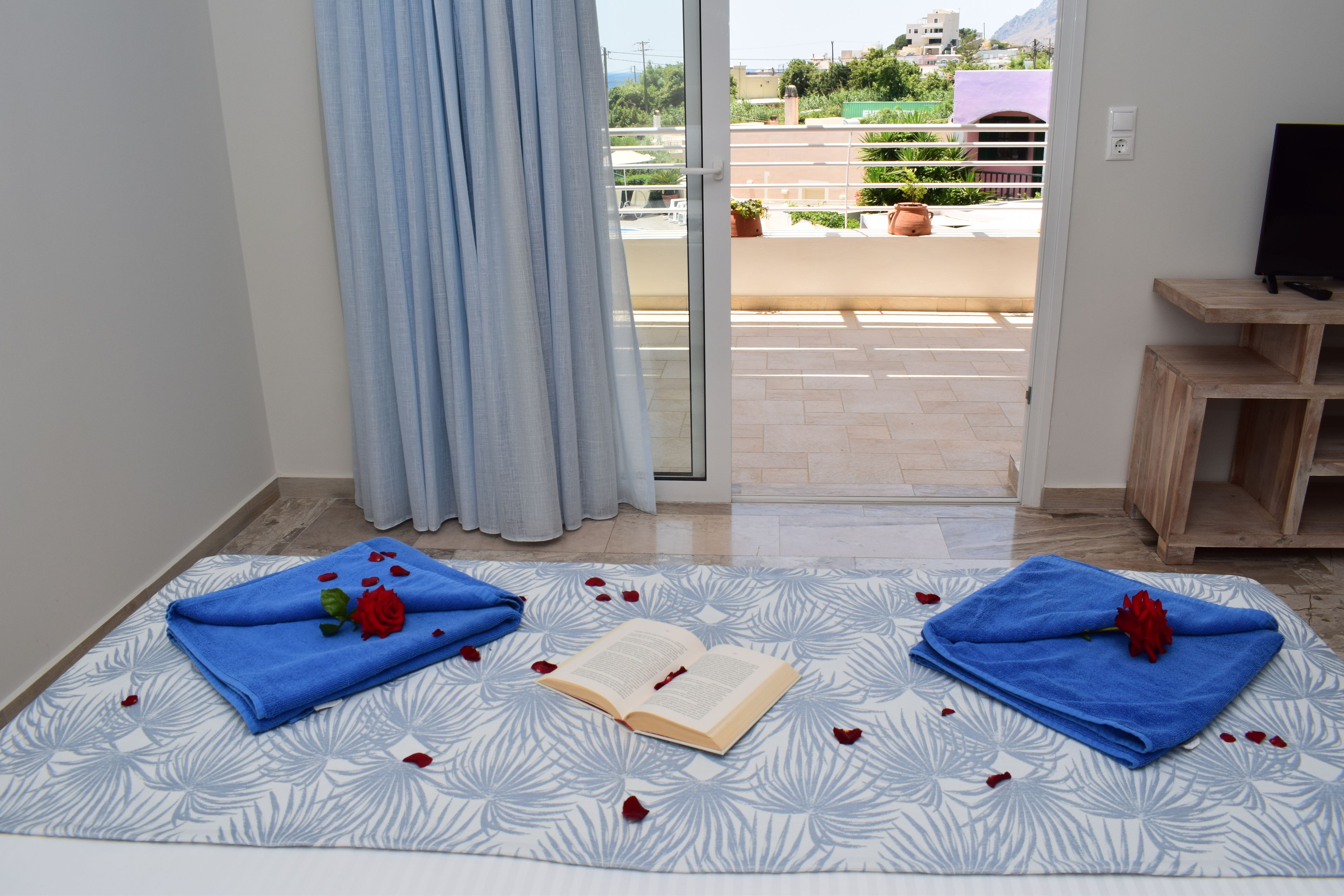 Una habitación con una cama, un libro y dos toallas decoradas con pétalos de rosa.
