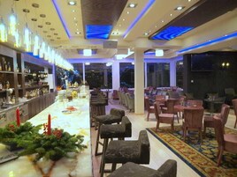 Un área de bar con una barra alargada, diversas opciones de asientos y una decoración con plantas.
