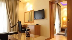 Ein Hotelzimmer mit Bett, Schreibtisch mit Vase, Flachbildfernseher und Spiegel.