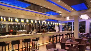 Eine Bar mit einer langen Theke, mehreren Barhocker und runden Tischen mit Stühlen.