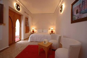 A bedroom with a bed, bedside tables, a red carpet, and a door leading to an outdoor area. - Riad Anais (Marrakech)