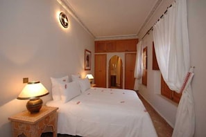 Ein Schlafzimmer mit einem Bett, Nachttischen, einer Lampe und Vorhängen.