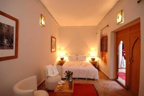 Ein Hotelzimmer mit Bett, Nachttischen, einem Sessel, einem kleinen Tisch mit Vase und einem roten Teppich.