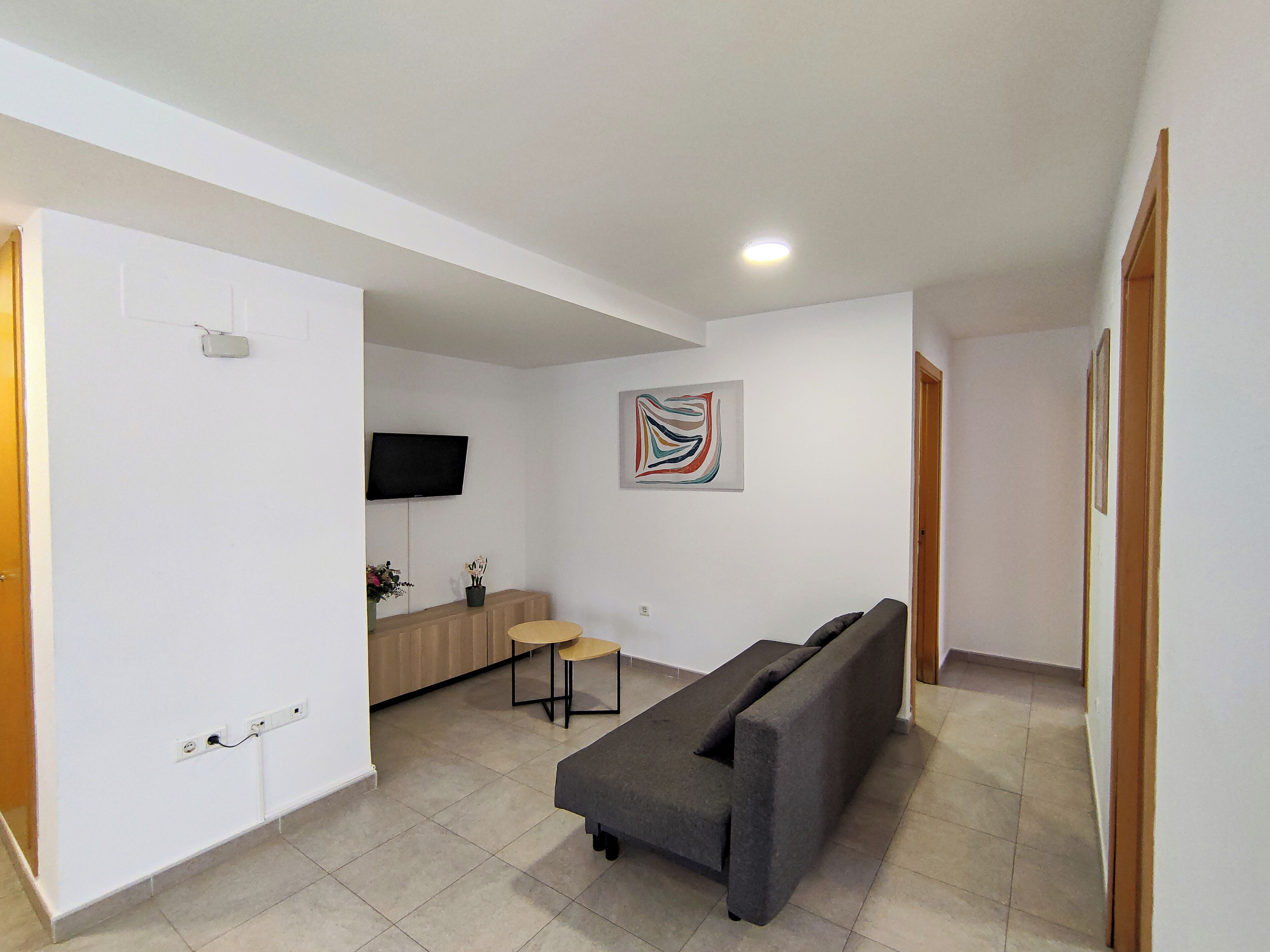 A modern living room with a grey sofa, a small round table, and a TV mounted on the wall.