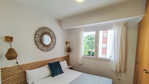 Un dormitorio con cama, un espejo redondo, una ventana con cortinas y un cabecero de madera.