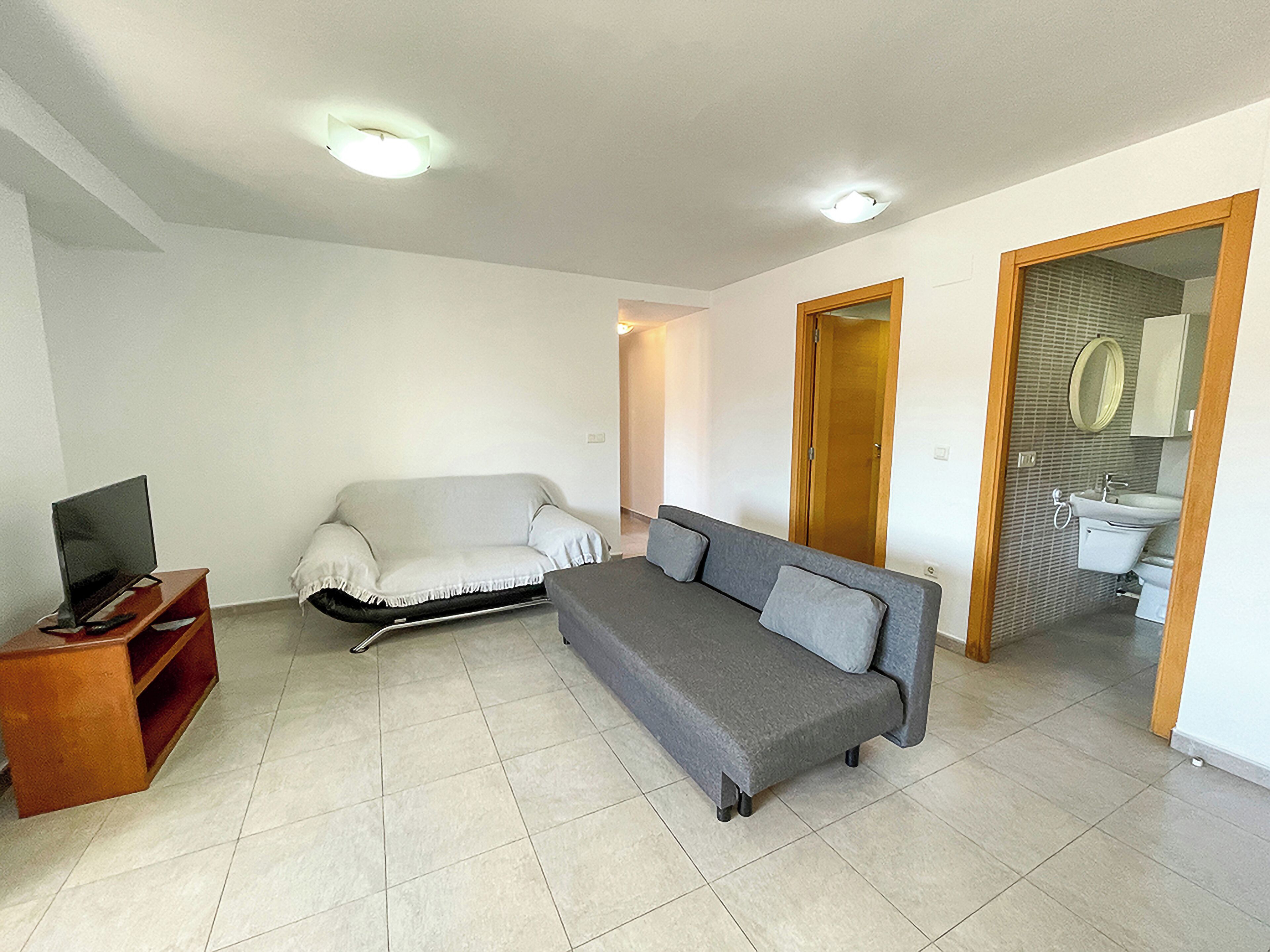 Un salon avec un canapé, un téléviseur posé sur un meuble en bois et une porte donnant sur une salle de bain.
