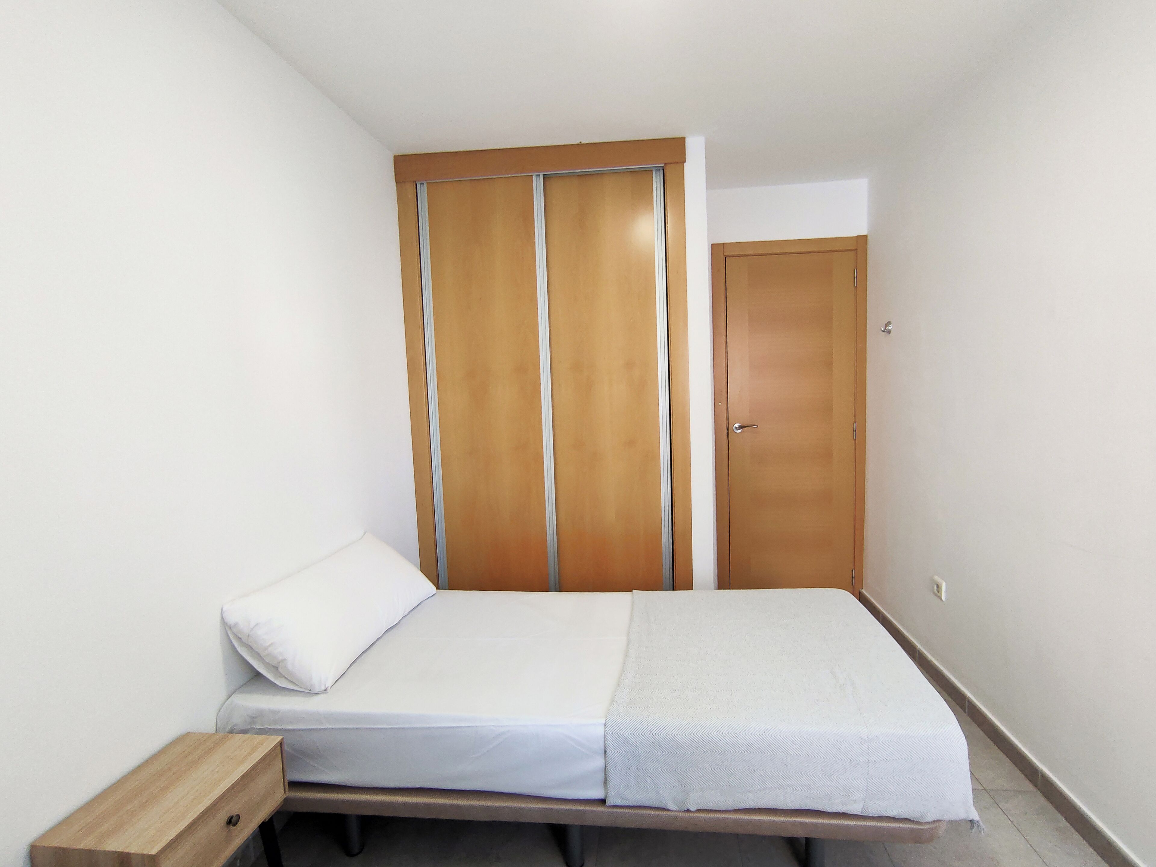 A bedroom with a bed, a wooden wardrobe, and a door.