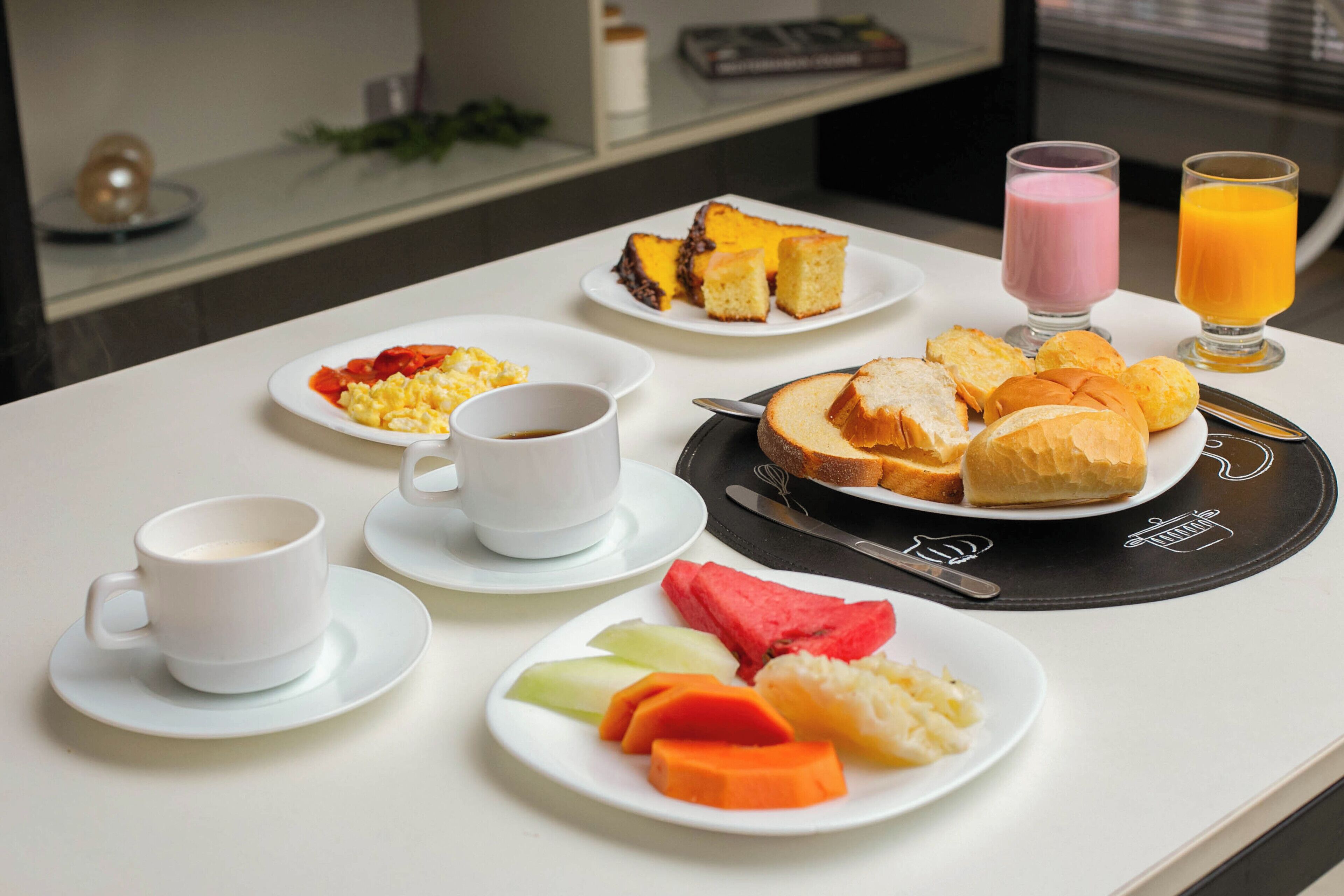 Una mesa de desayuno con platos de comida, tazas y vasos de jugo.
