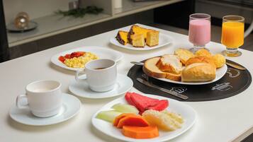 Una mesa de desayuno con platos de comida, tazas y vasos de jugo.