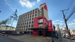 Een hotel met meerdere verdiepingen, met een opvallende rode en beige gevel, een ruime entree met een glazen deur en een parkeerplaats met aangegeven parkeerplaatsen.