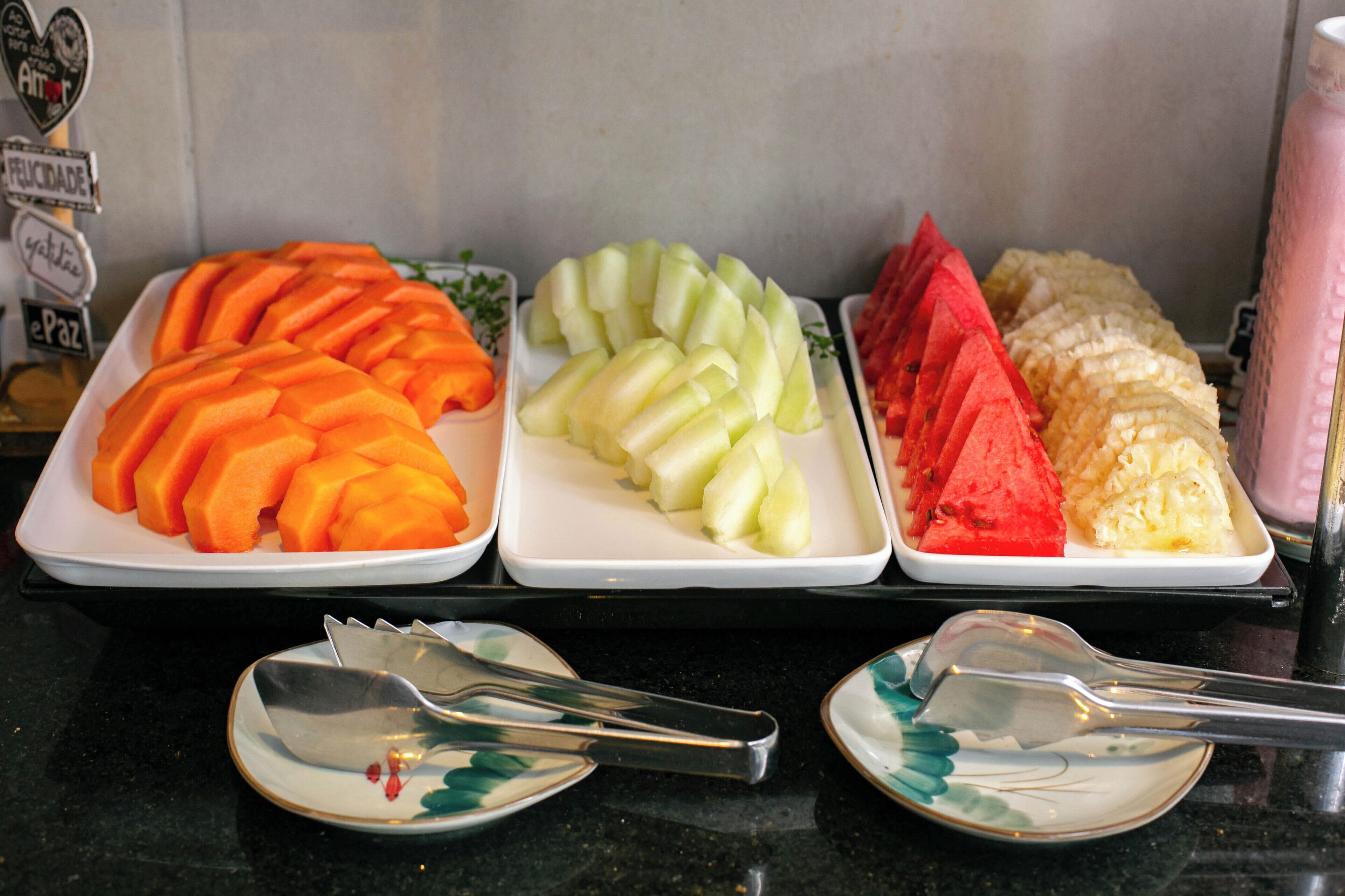 Three trays of sliced fruits on a counter.