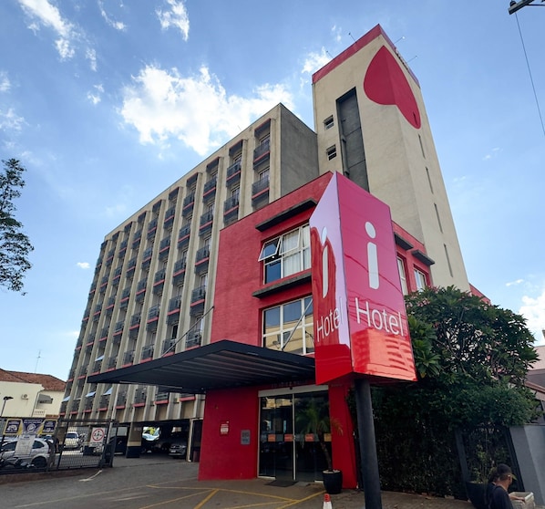 Een hotel met een gevel in rood en beige, met meerdere balkons en een opvallend 'Hotel' bord.