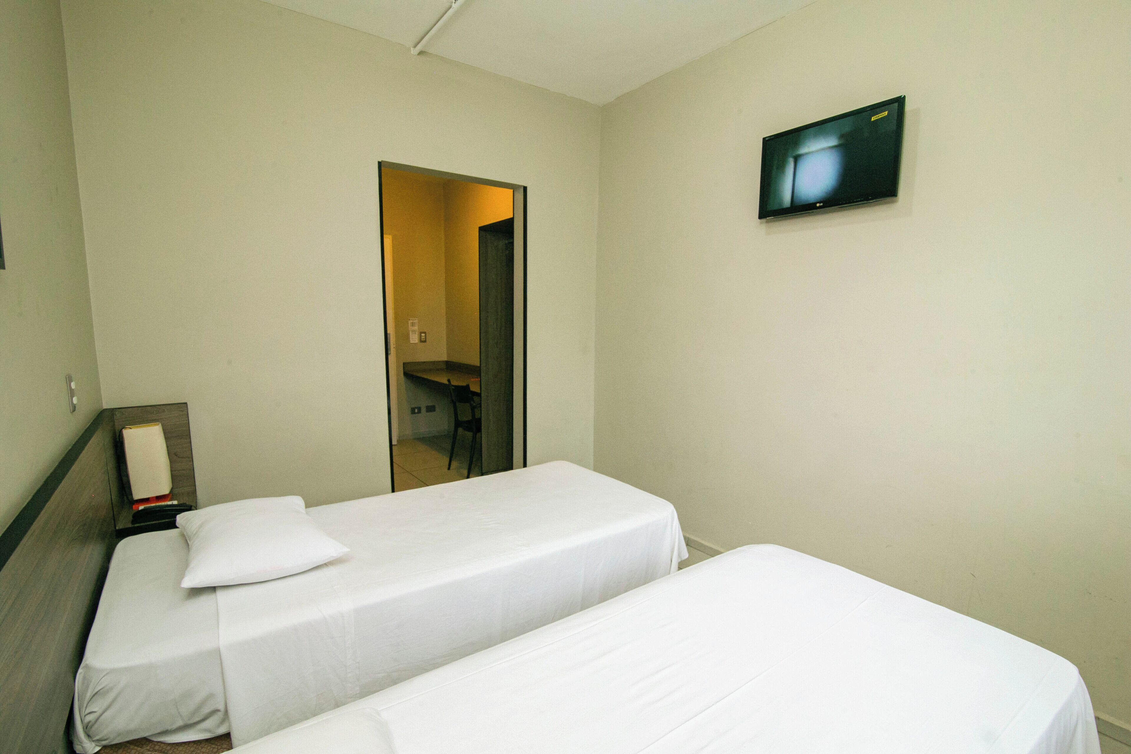 A hotel room with two single beds, a flat-screen TV mounted on the wall, and a door leading to a bathroom.