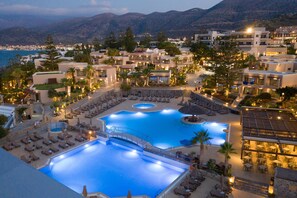A resort with multiple swimming pools, sun loungers, and a view of the sea.