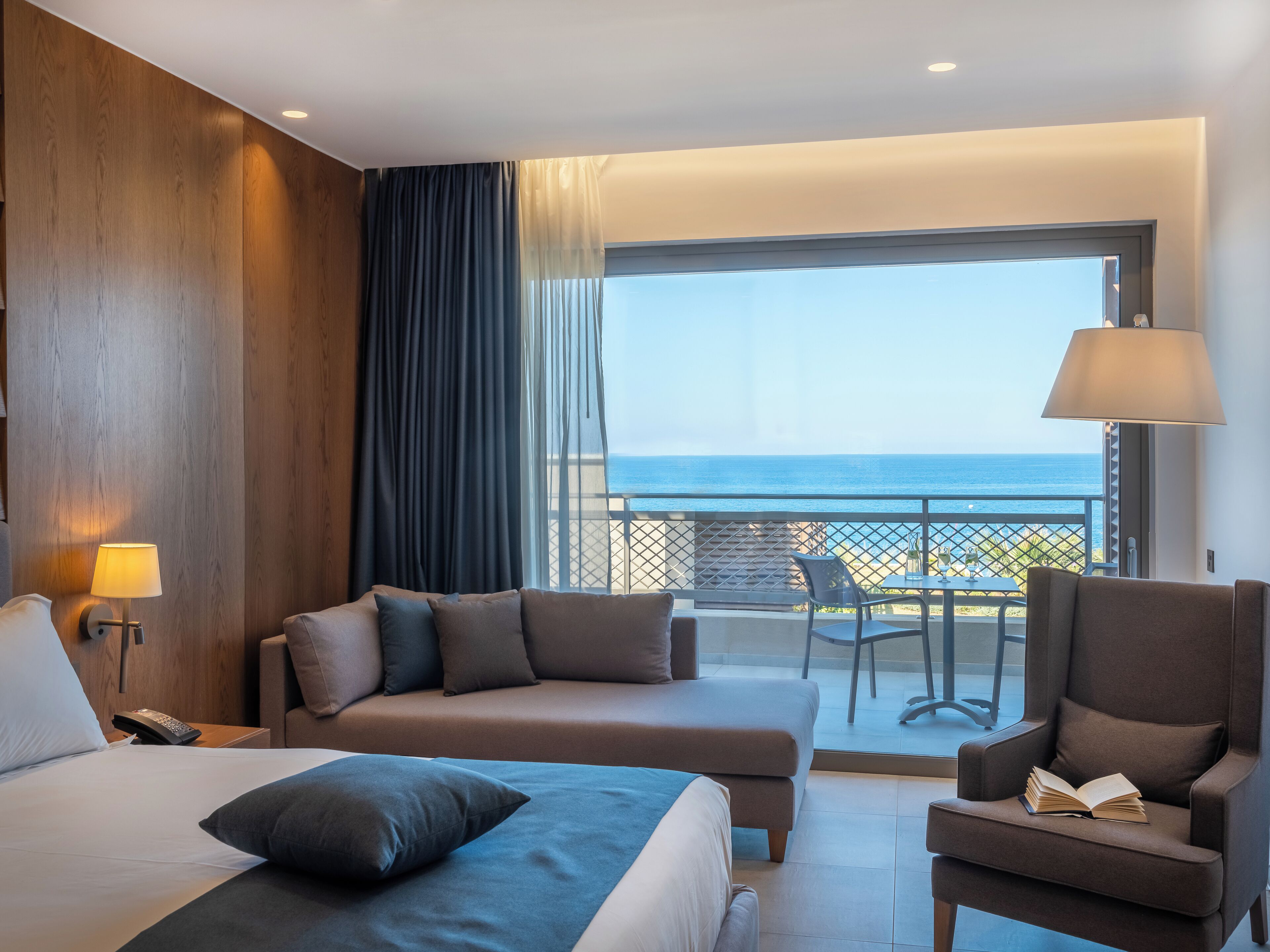 Een hotelkamer met een bed, een bank, een stoel, een tafel en uitzicht op zee.