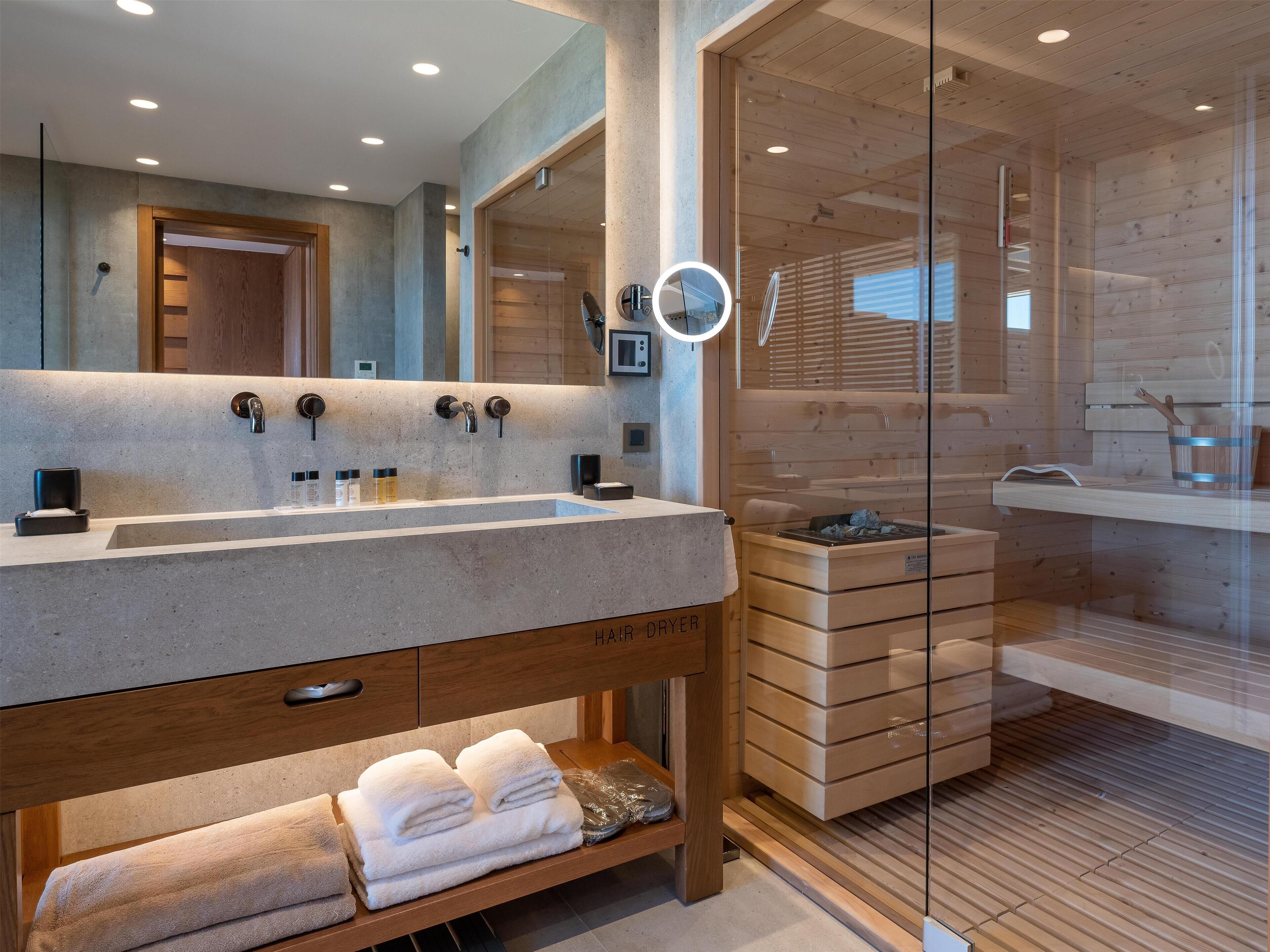 A modern bathroom with a large sink, a mirror, and a wooden sauna area.