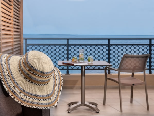 A balcony with a view of the sea, a table with drinks, and a chair.