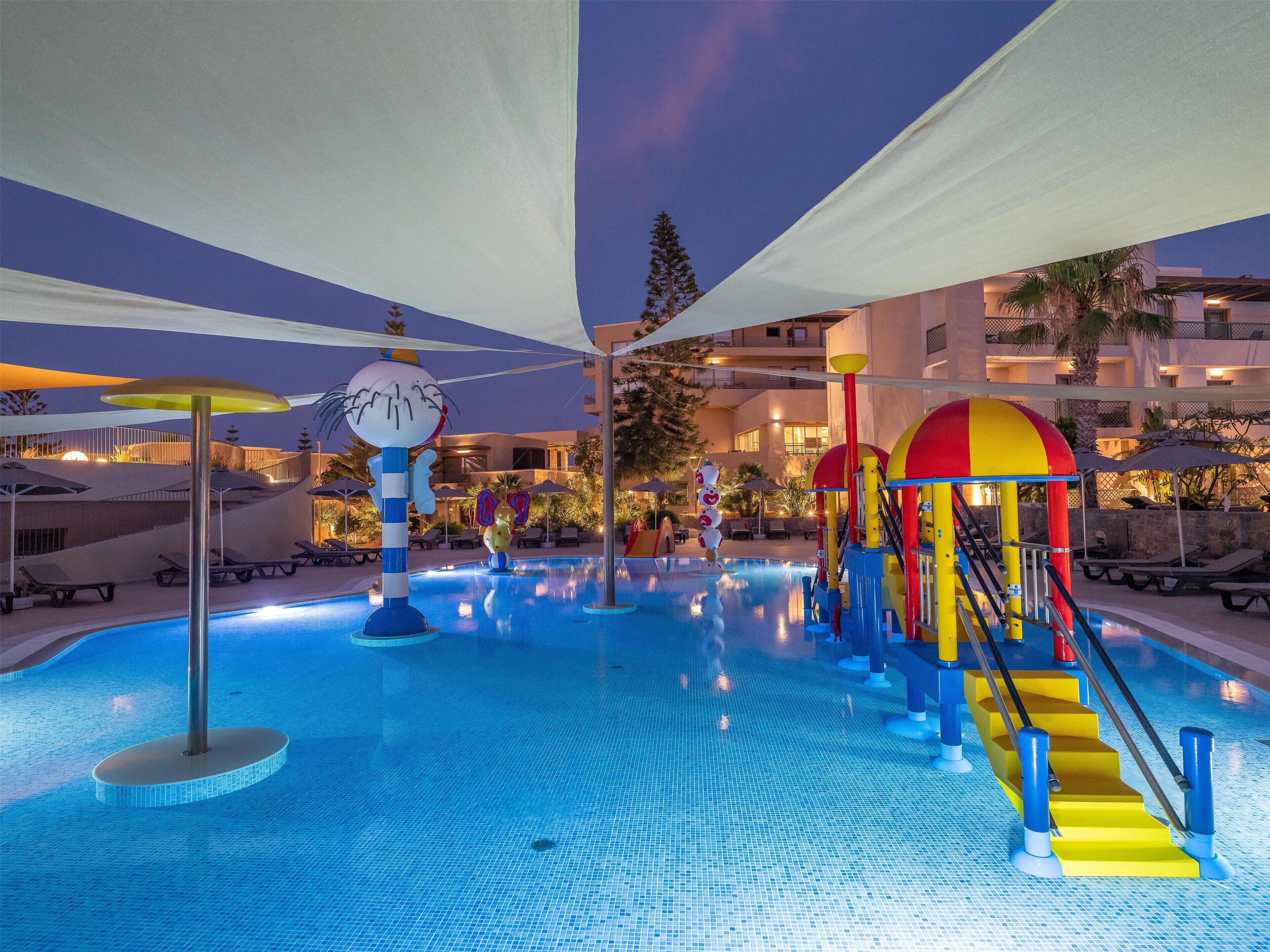 A swimming pool area with a slide, sun umbrellas, and lounge chairs.