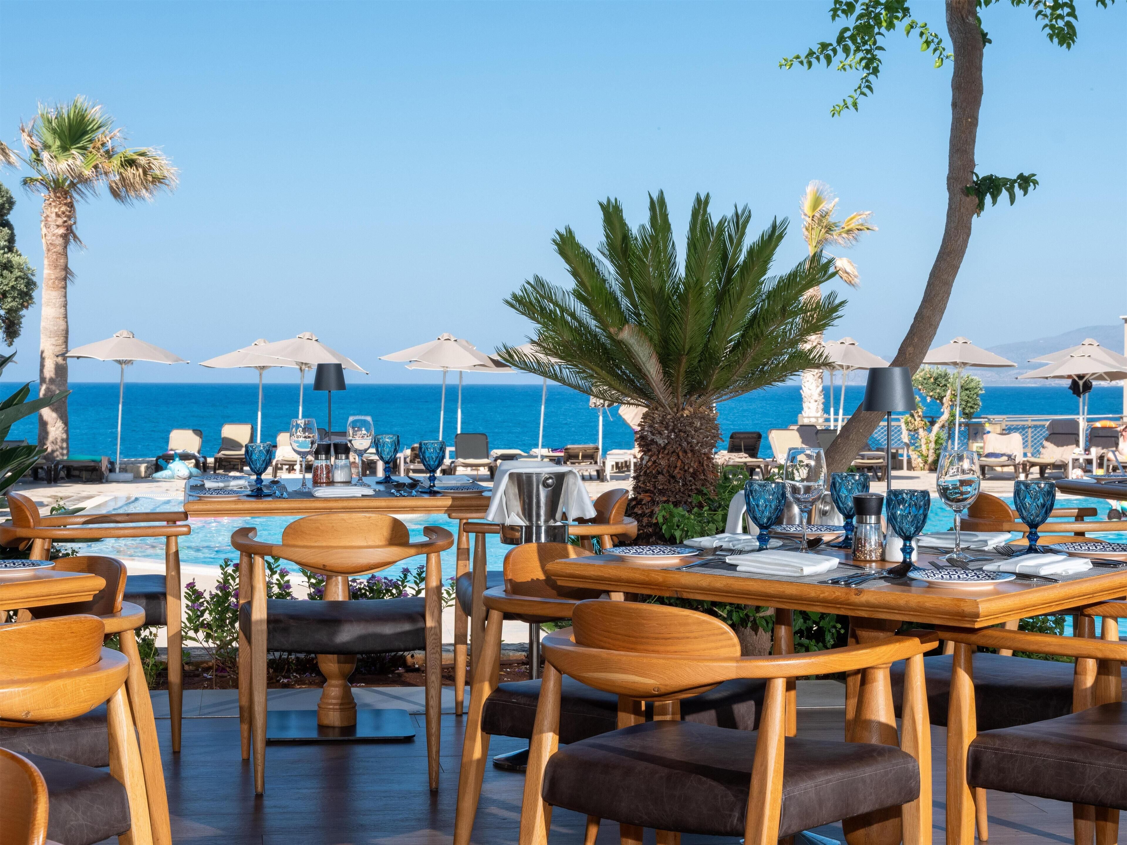 A seaside restaurant with outdoor seating, umbrellas, and a view of the ocean.