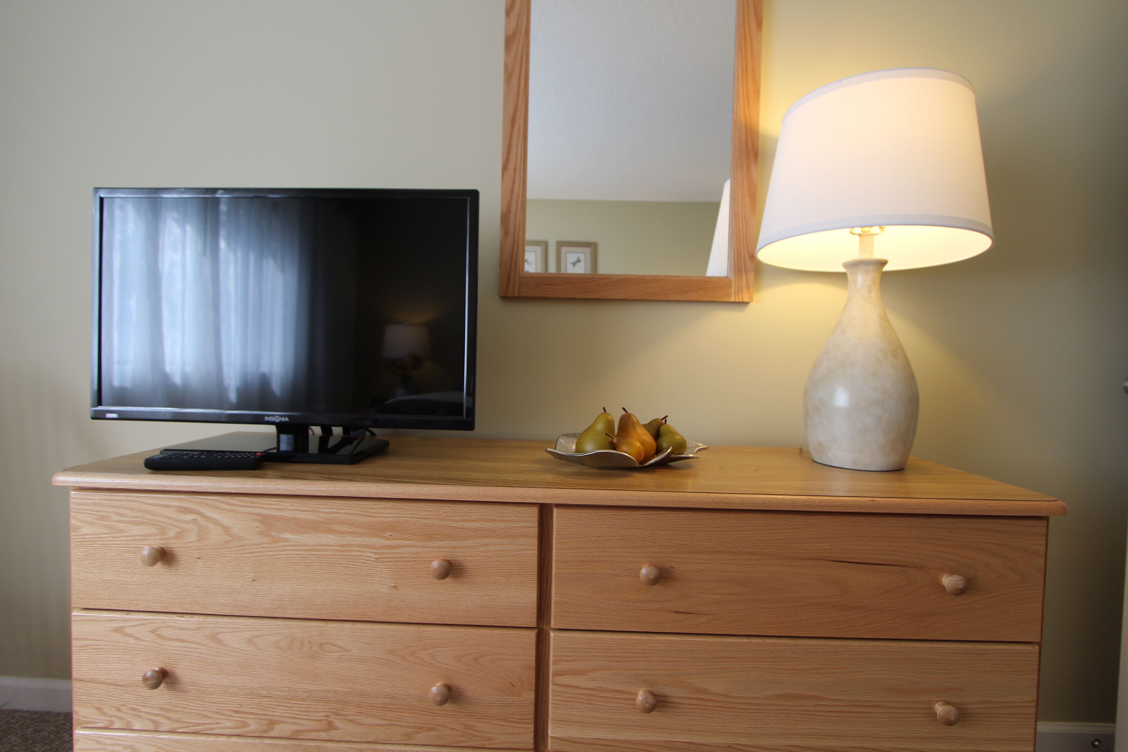 Une commode en bois, sur laquelle sont posés un téléviseur à écran plat, une lampe et un bol décoratif.