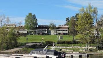 A lakeside view with a dock, boats, and a building with multiple windows and a flat roof.