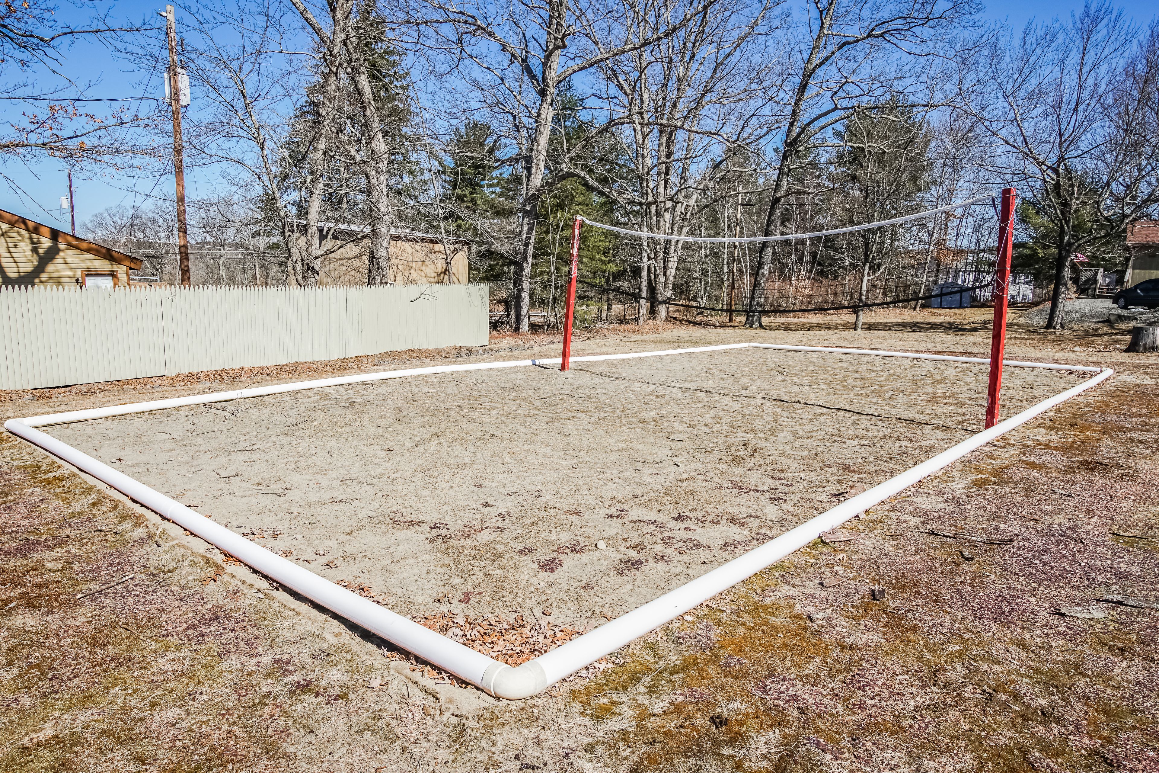 Un terrain de volley-ball avec un filet, entouré d’une clôture en bois et d’arbres.