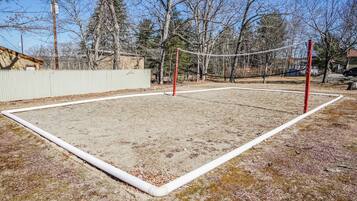 Un terrain de volley-ball avec un filet, entouré d’une clôture en bois et d’arbres.