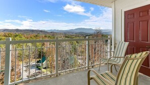 A balcony with a view of a mountainous landscape, a red door, and two striped chairs. - Sunrise Ridge Resort by Coolvacay (Pigeon Forge)
