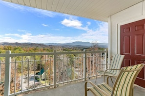 A balcony with a view of a mountainous landscape, a red door, and two striped chairs.
