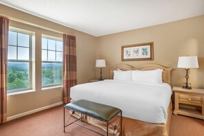 A hotel room with a large bed, two bedside tables with lamps, a bench, and a view of greenery through the windows. - Sunrise Ridge Resort by Coolvacay (Pigeon Forge)