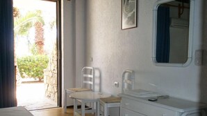 A room with a bed, a white dresser, two chairs, a small table, and a window with a view of greenery outside. - Avra Palm (Ierapetra)