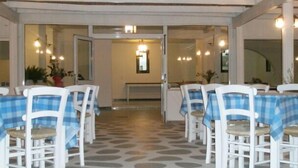 A restaurant with white chairs and blue checkered tablecloths, a patterned floor, and a view of the interior through glass doors. - Avra Palm (Ierapetra)