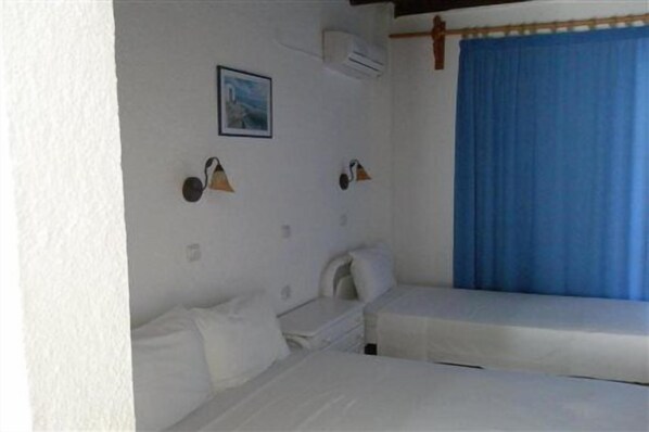 A room with two beds, a wall-mounted air conditioner, and a blue curtain. - Avra Palm (Ierapetra)