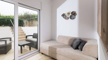 A modern living room with a beige sofa, a glass door leading to an outdoor area, and a wall decoration.