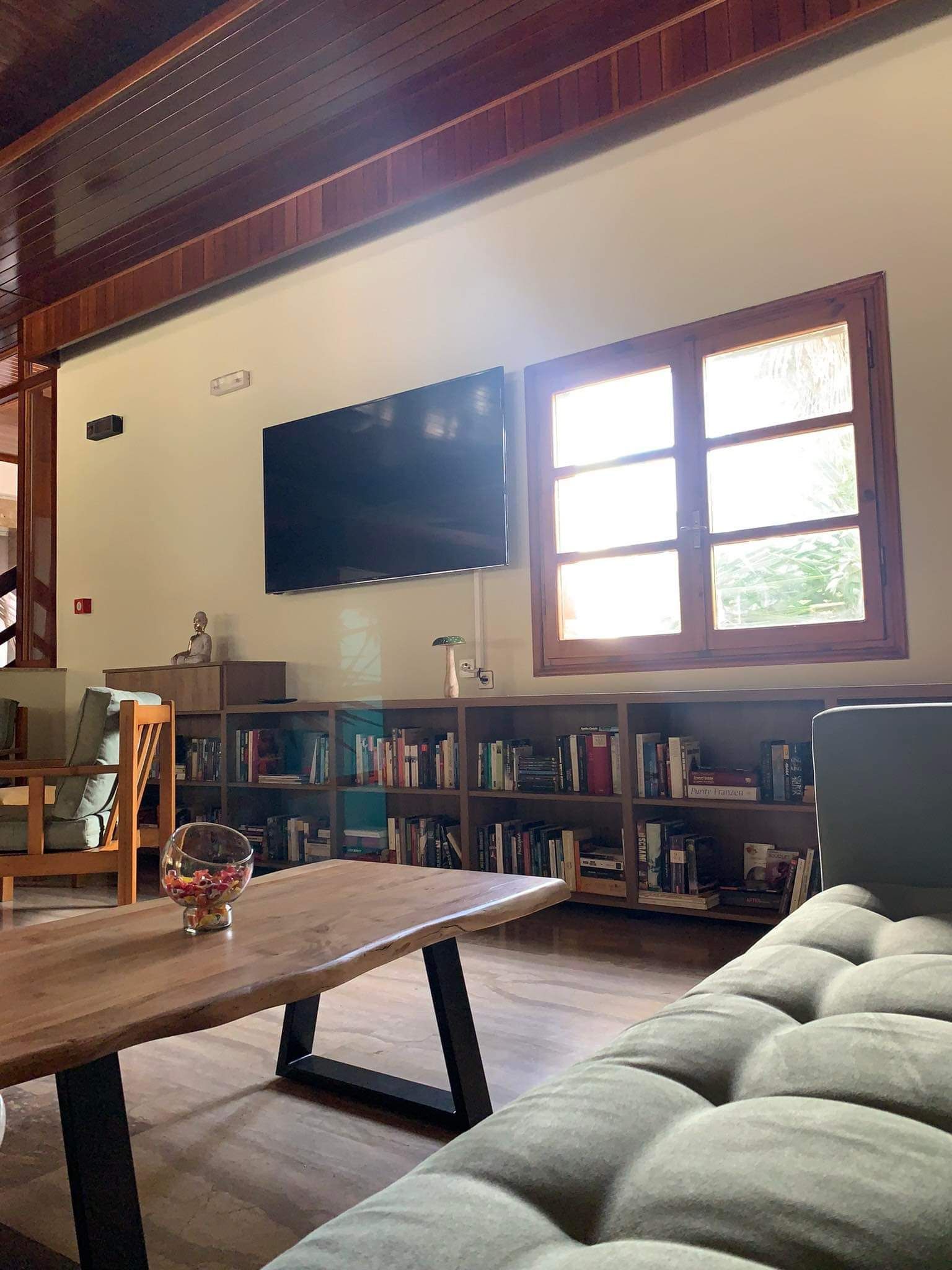 Una sala de estar acogedora con un televisor de pantalla plana montado en la pared, una mesa de centro de madera, un sofá cómodo y una estantería llena de libros.