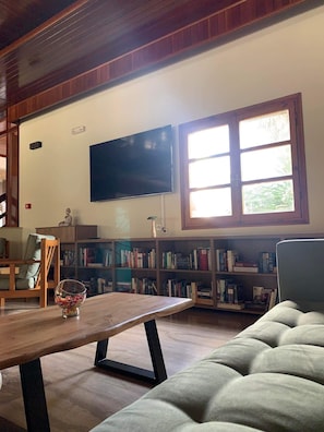 Una sala de estar acogedora con un televisor de pantalla plana montado en la pared, una mesa de centro de madera, un sofá cómodo y una estantería llena de libros.