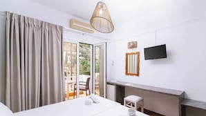 A hotel room with a bed, a desk, a chair, a television, and a sliding glass door to the outside. - Elea Terra Hotel (Faistos)