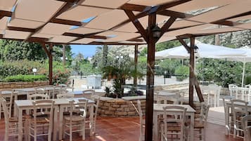 Une terrasse extérieure avec des tables et des chaises blanches, des murs en pierre et une structure en forme de pergola.